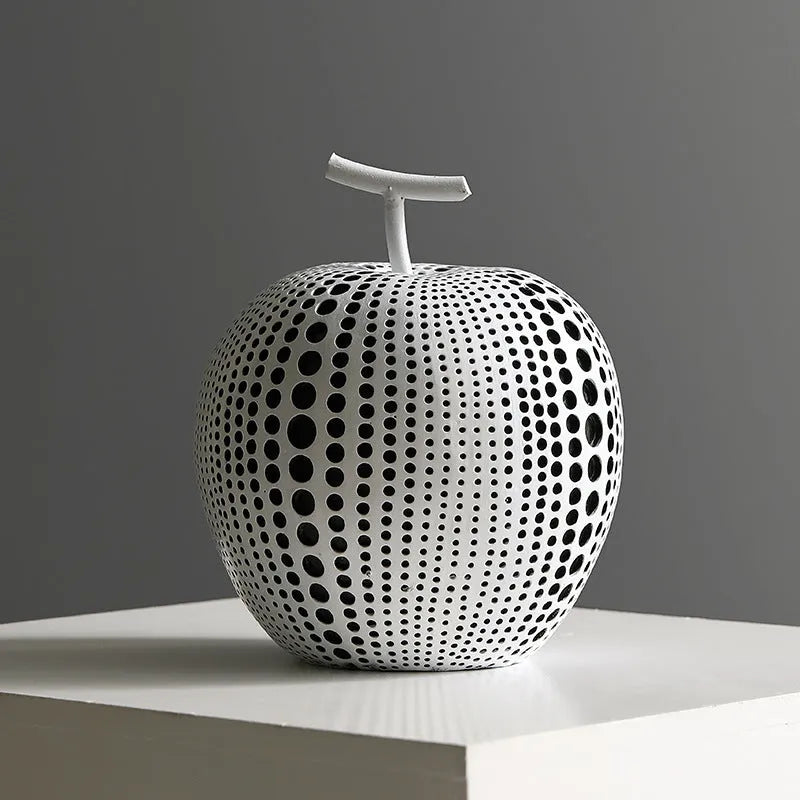 A tall black resin vase and a low white resin apple decoration on a wooden table.
