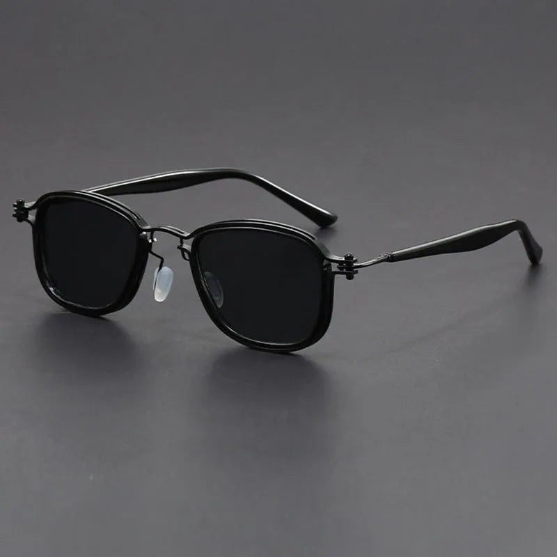 Retro square sunglasses with black gold frames and grey AC lenses on a wooden surface.