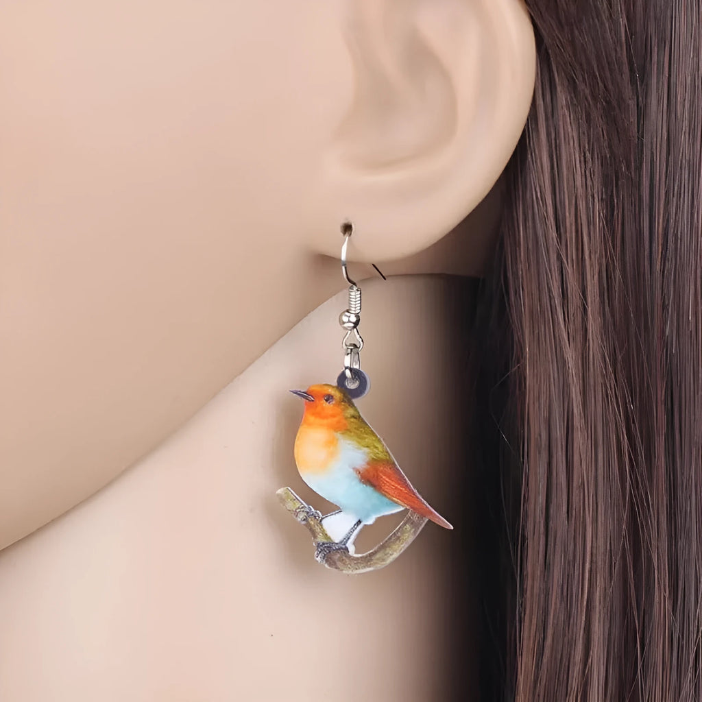 Pair of blue and white acrylic pendant earrings featuring a printed titmouse bird and snake design on geometric shapes.