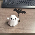 Miniature white ghost dog statue holding a bat, a small resin Halloween ornament on a wooden surface.