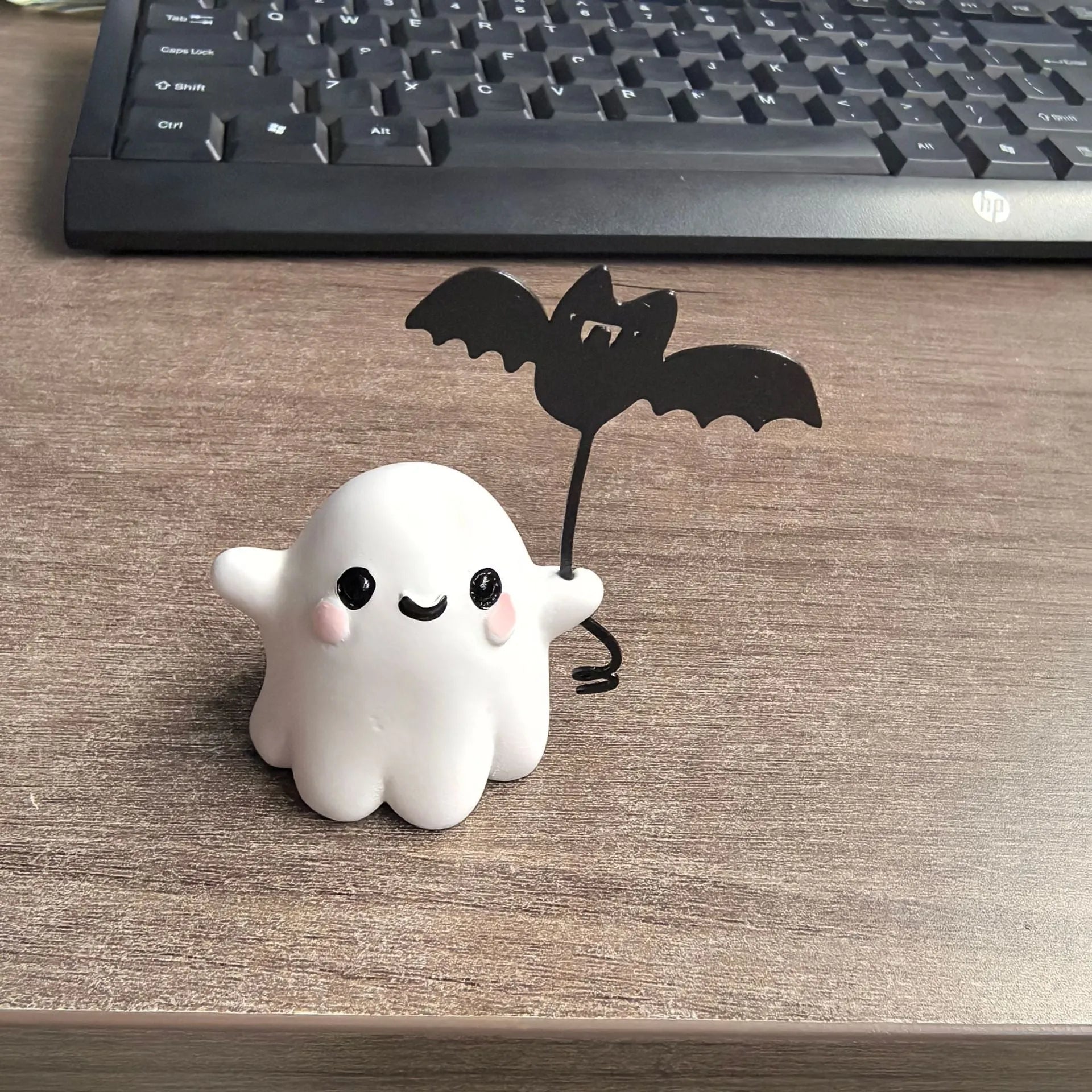 Miniature white ghost dog statue holding a bat, a small resin Halloween ornament on a wooden surface.