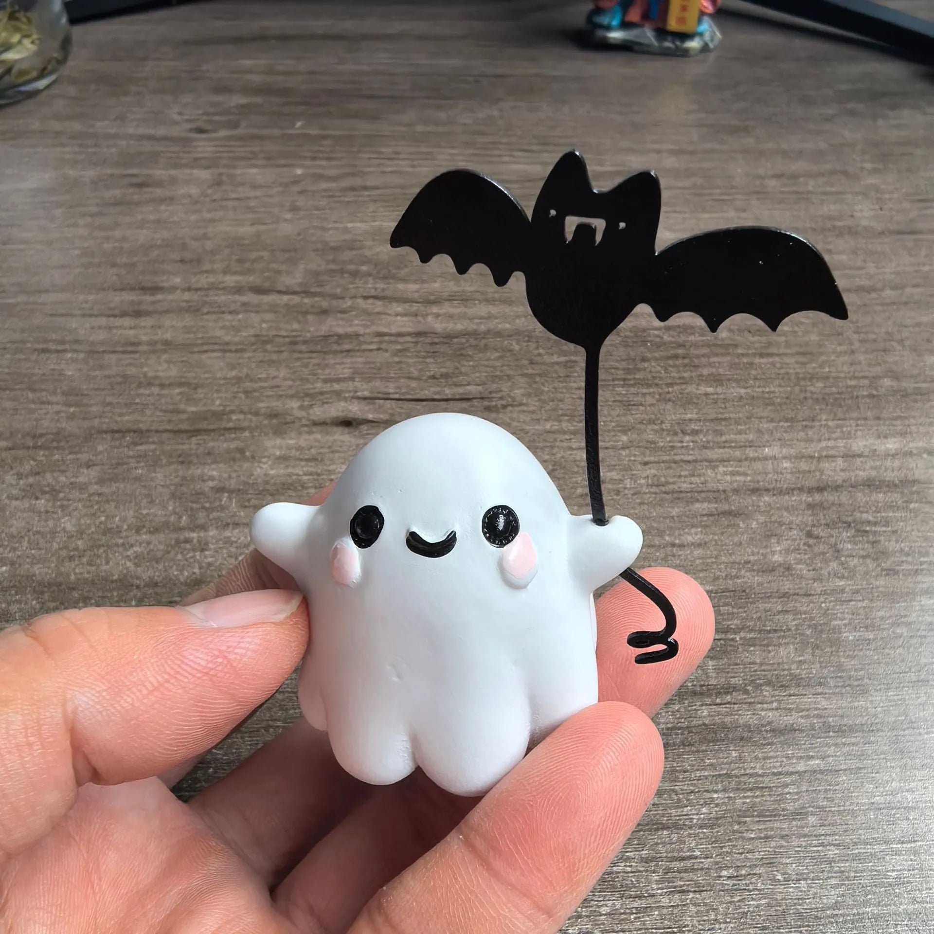 Miniature white ghost dog statue holding a bat, a small resin Halloween ornament on a wooden surface.
