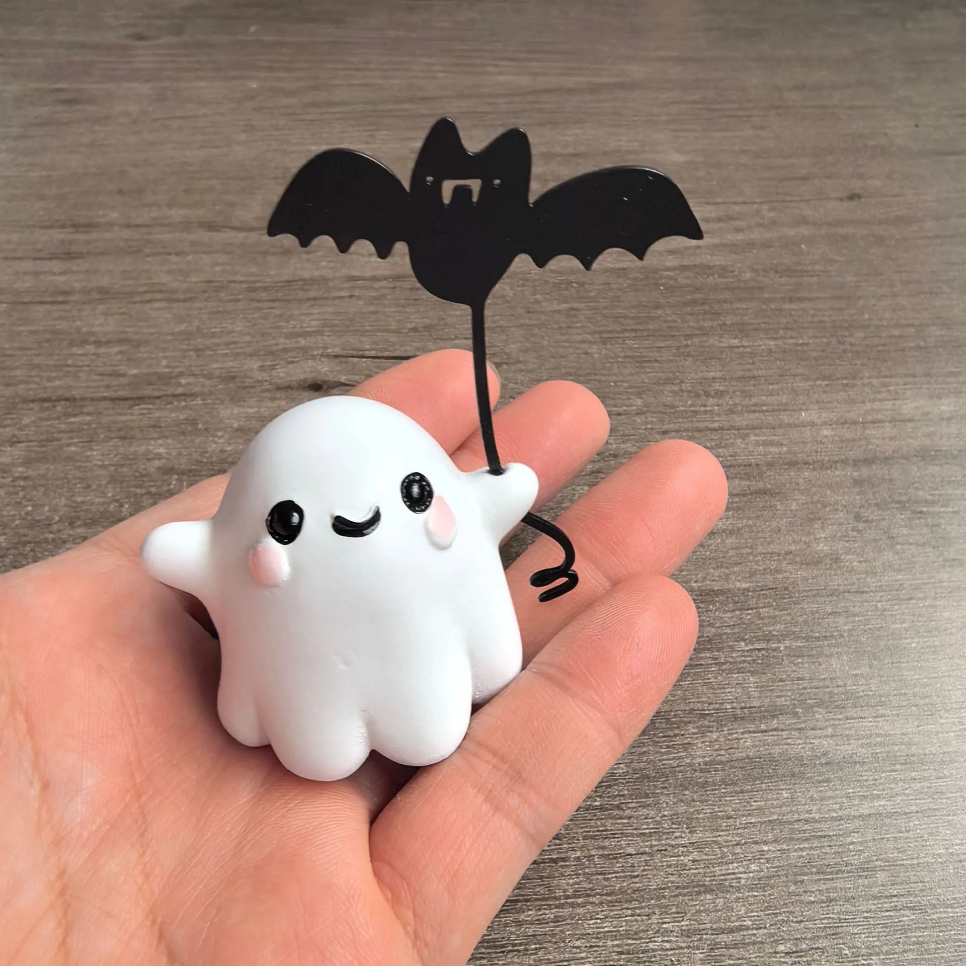 Miniature white ghost dog statue holding a bat, a small resin Halloween ornament on a wooden surface.