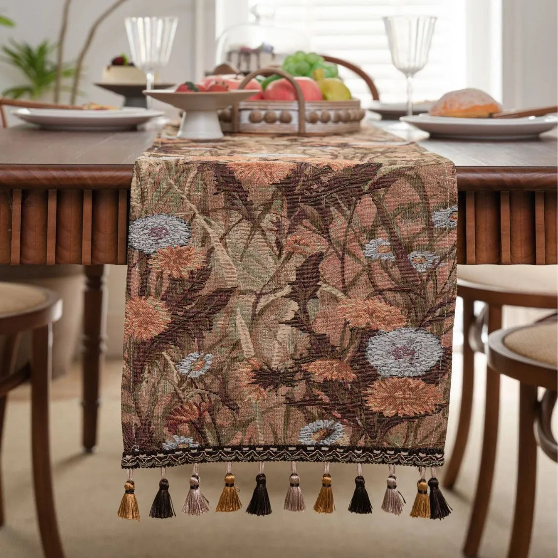 Beige jacquard table runner with floral leaf pattern and long tassels draped on a wooden dining table.