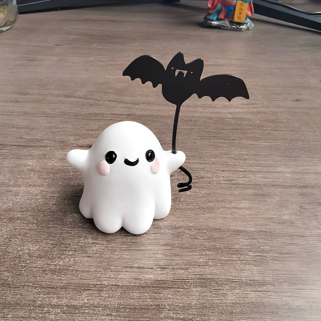 Miniature white ghost dog statue holding a bat, a small resin Halloween ornament on a wooden surface.