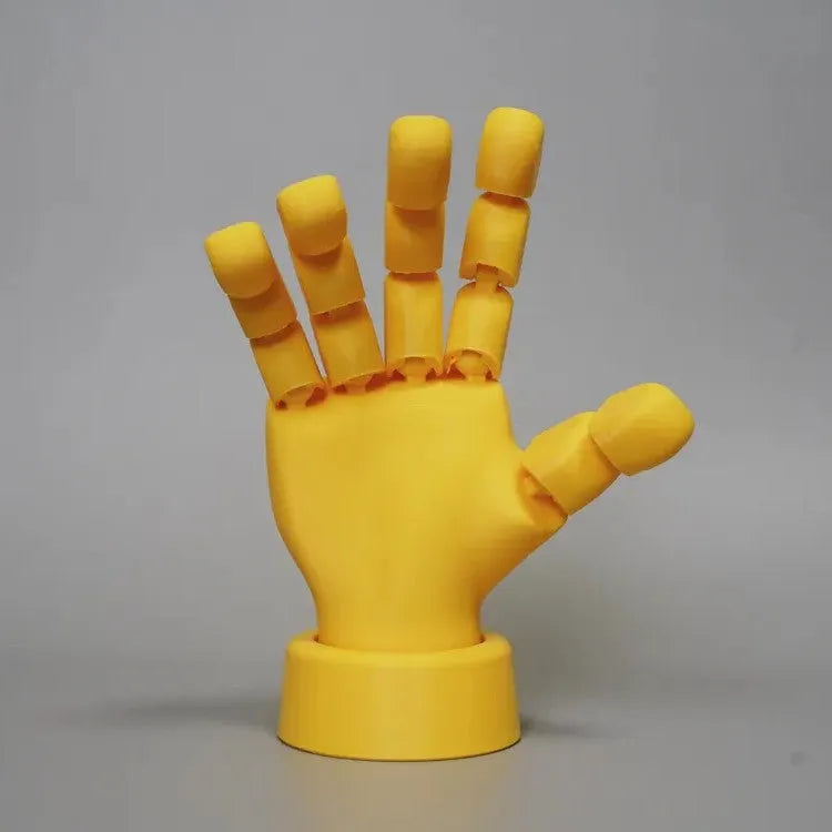 Yellow articulated hand prop ornament with movable joints on a desk, showing poseable fingers and measuring 5cm wide.