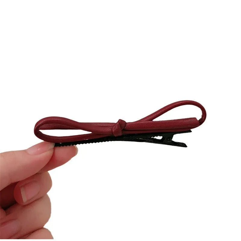 Wine red genuine leather bow hair barrette with metal clip on a white background.
