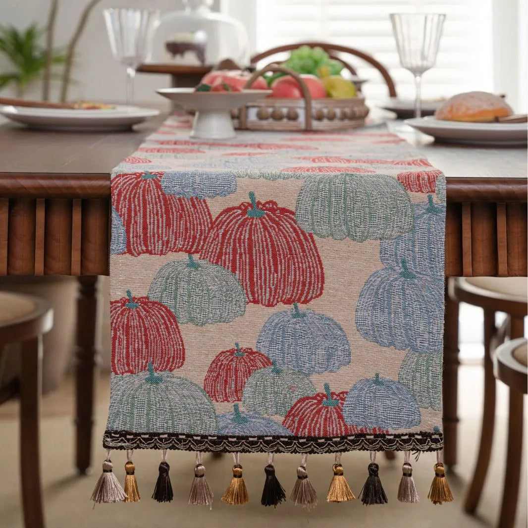 Beige jacquard table runner with floral leaf pattern and long tassels draped on a wooden dining table.