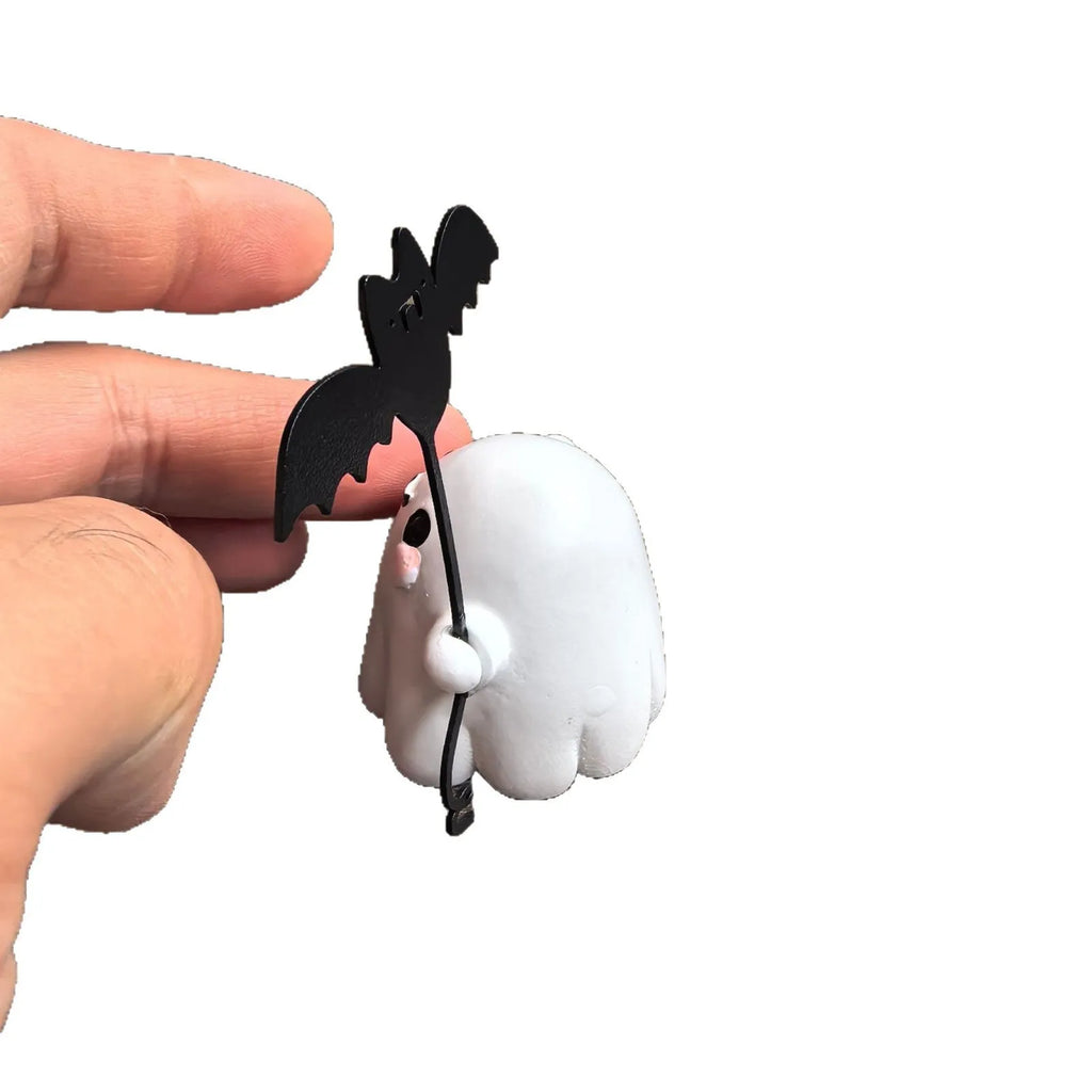 Miniature white ghost dog statue holding a bat, a small resin Halloween ornament on a wooden surface.