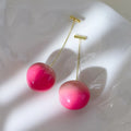 A pair of glossy, colourful acrylic earrings shaped like juicy peaches, on copper posts.