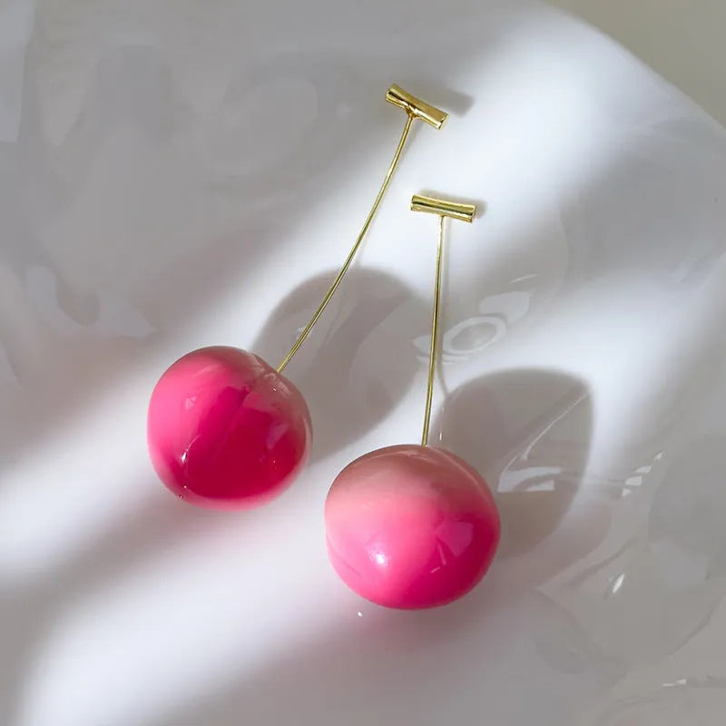 A pair of glossy, colourful acrylic earrings shaped like juicy peaches, on copper posts.