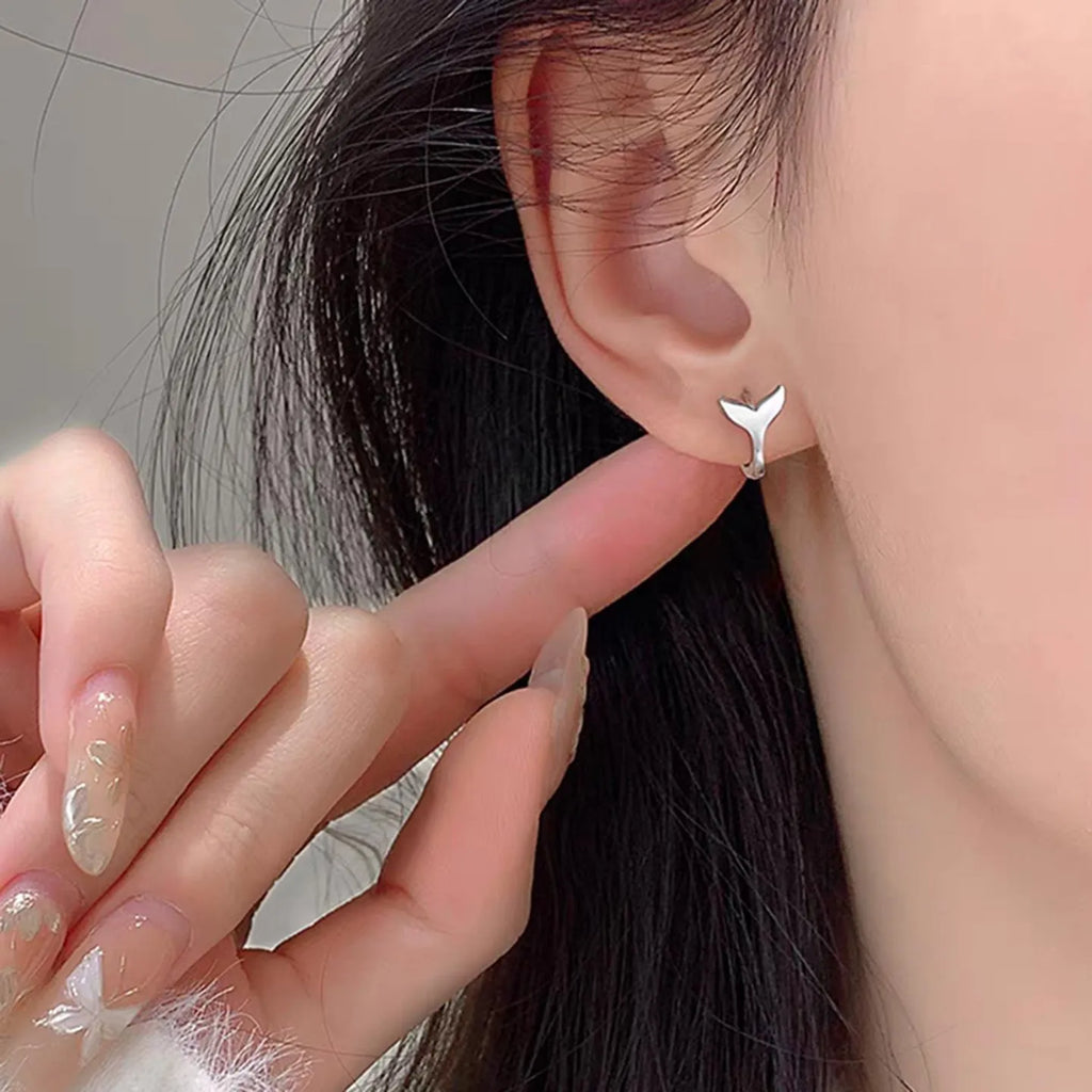 A pair of simple women's fishtail earrings in a gold tone finish on a copper base.