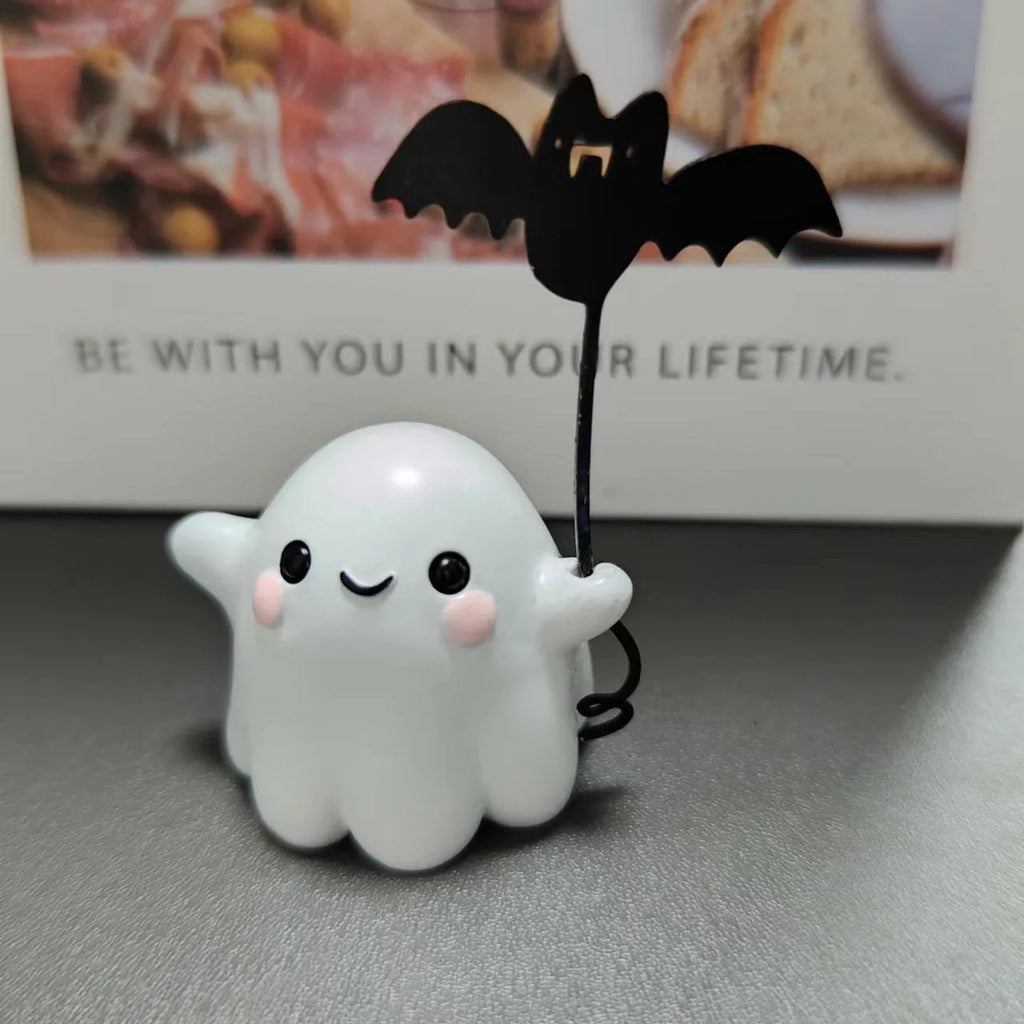 Miniature white ghost dog statue holding a bat, a small resin Halloween ornament on a wooden surface.