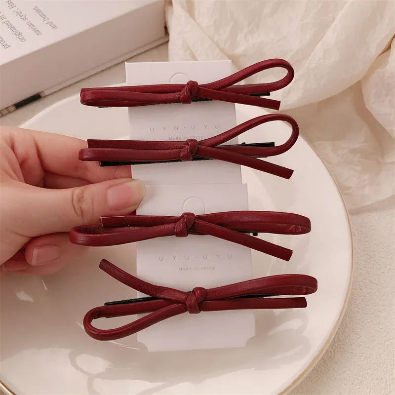 Wine red genuine leather bow hair barrette with metal clip on a white background.