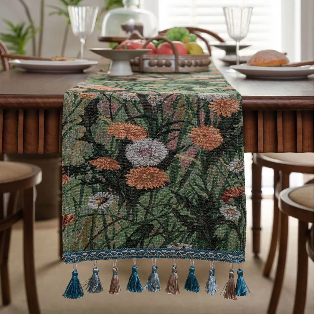 Beige jacquard table runner with floral leaf pattern and long tassels draped on a wooden dining table.