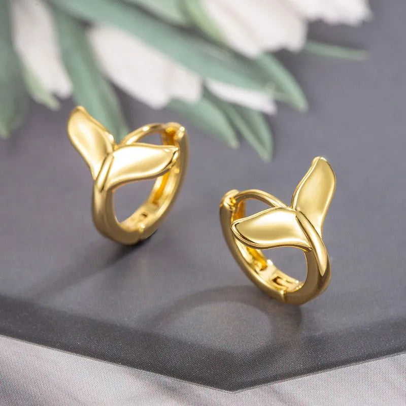 A pair of simple women's fishtail earrings in a gold tone finish on a copper base.