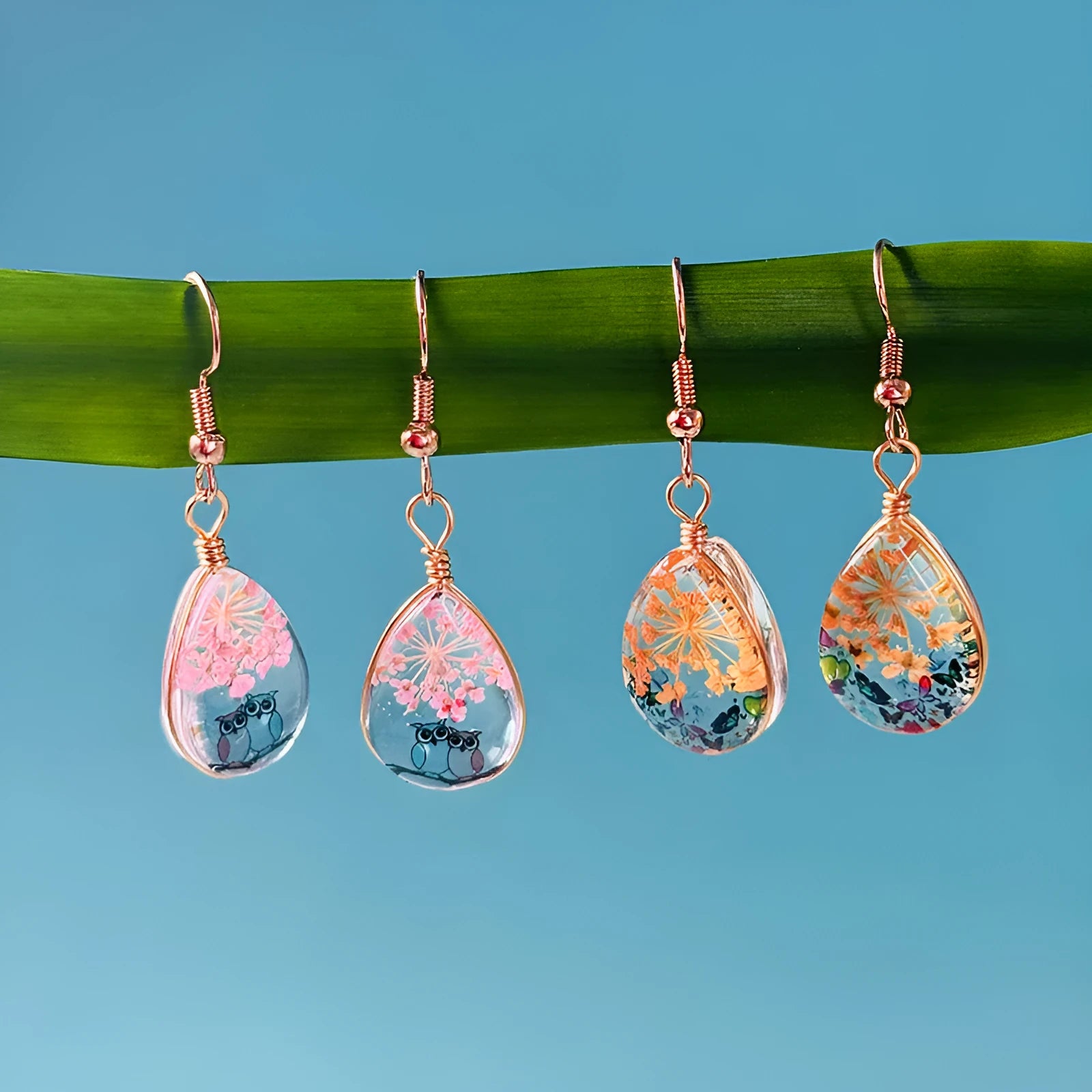 Water drop-shaped glass eardrops earrings with owl motif in ginger yellow and pink coloured glaze on a light background
