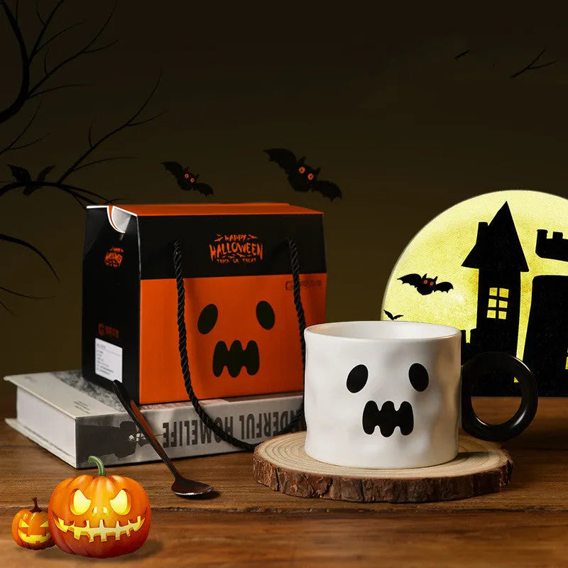 Orange ceramic pumpkin-shaped mug with handle on a table beside a dessert spoon and gift box.