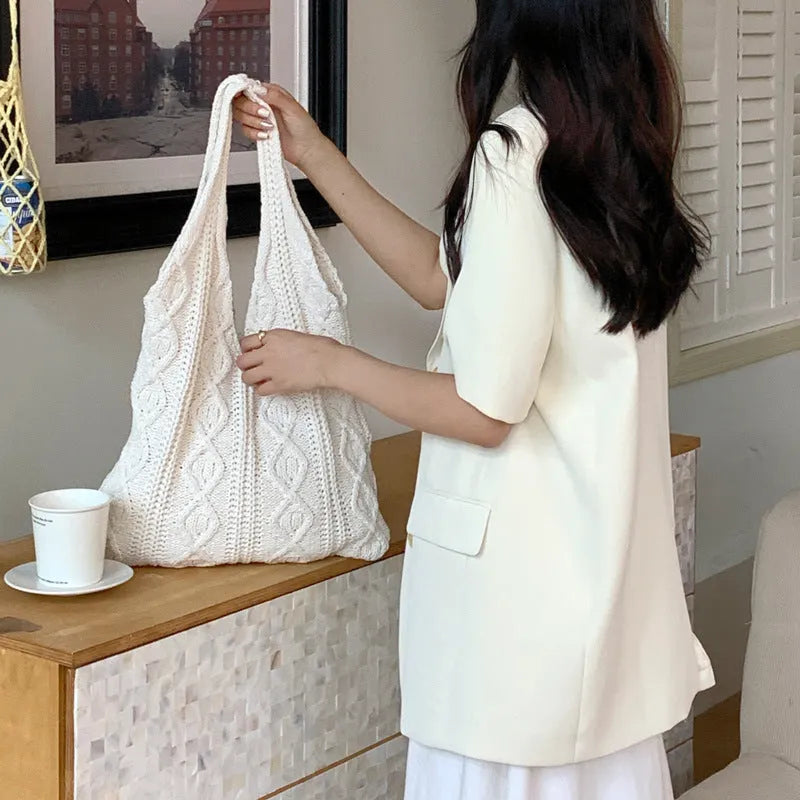 Light brown crochet knit tote bag with double shoulder straps on a wooden table.