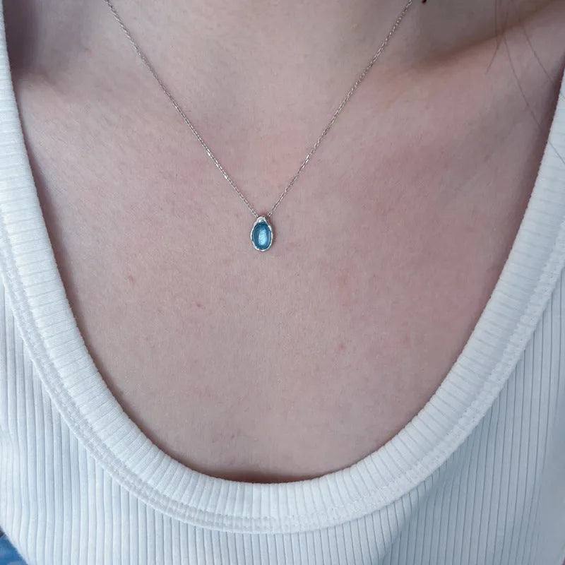 Close-up of a navy blue water drop pendant necklace with a platinum-colour finish on a textured cross chain.