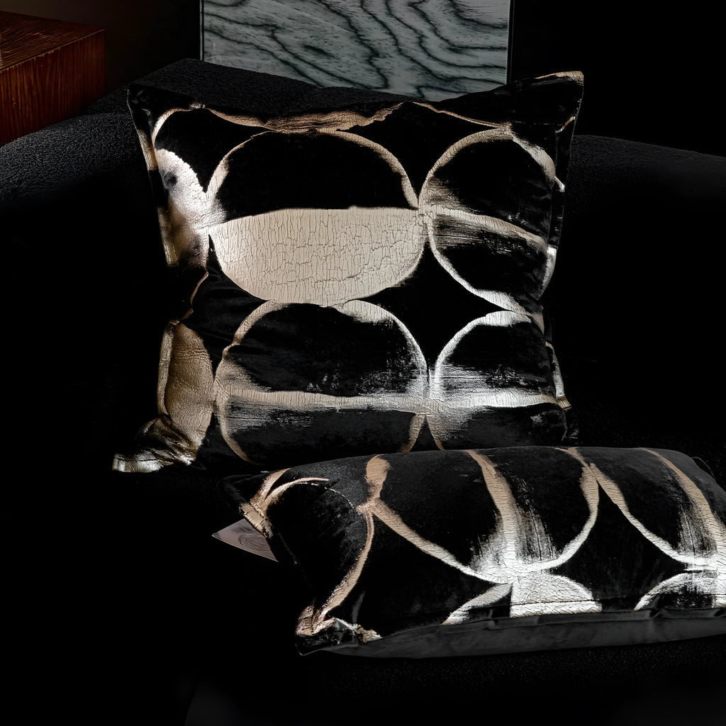 Black and gold abstract pattern decorative square and waist pillow cushions on a grey sofa.