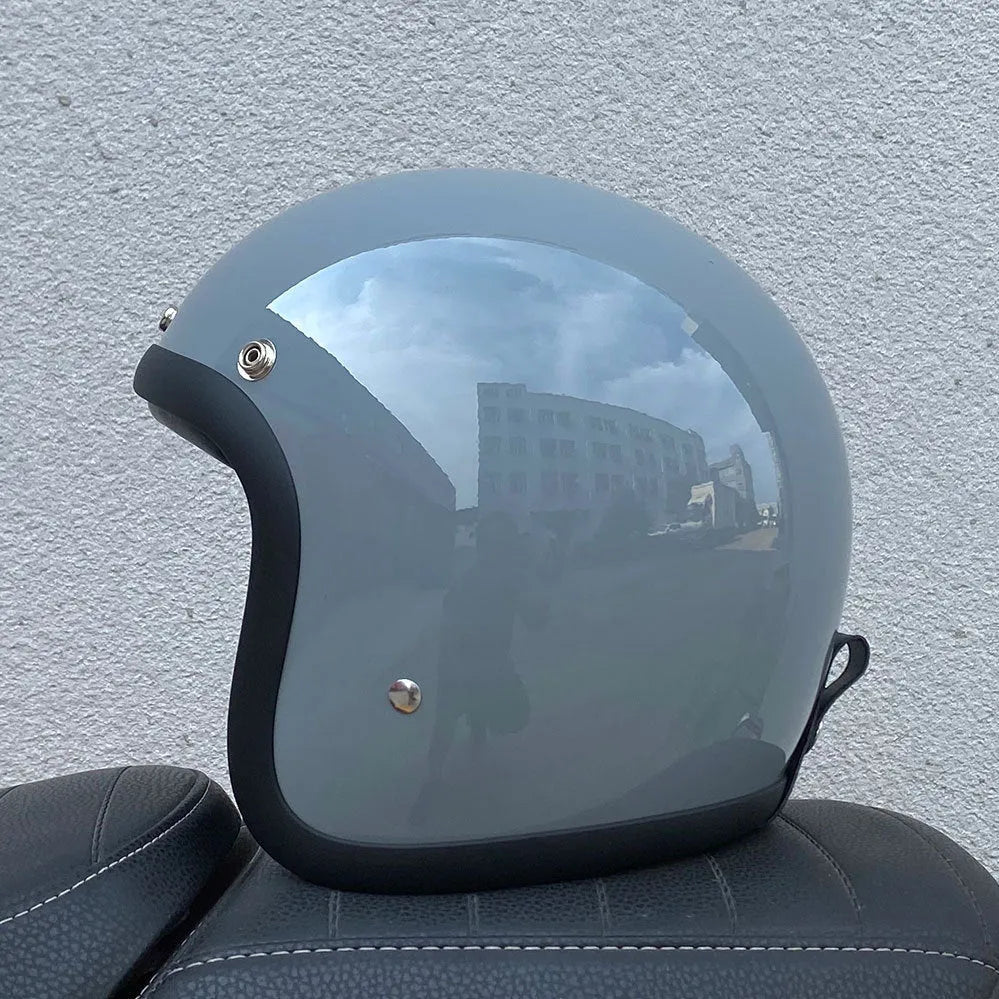 Retro-style half motorcycle helmet in fibreglass, shown in Cement Grey colour on a stand.
