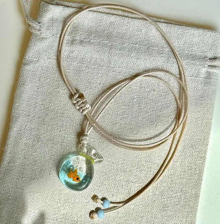 Women's necklace with a blue hand-painted fish charm on a beige cotton and linen clavicle chain.