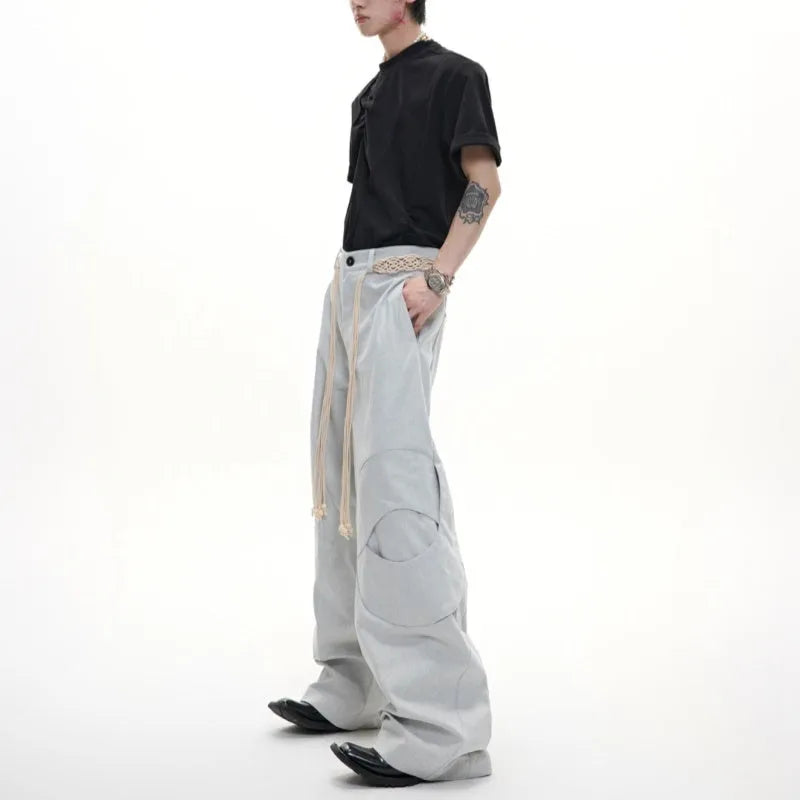 Men's dark blue straight-leg jeans showing loose fit, belt stitching with tassel, and zip pocket decorations.