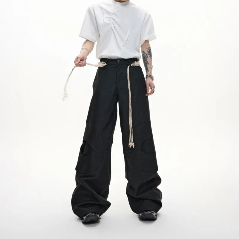 Men's dark blue straight-leg jeans showing loose fit, belt stitching with tassel, and zip pocket decorations.