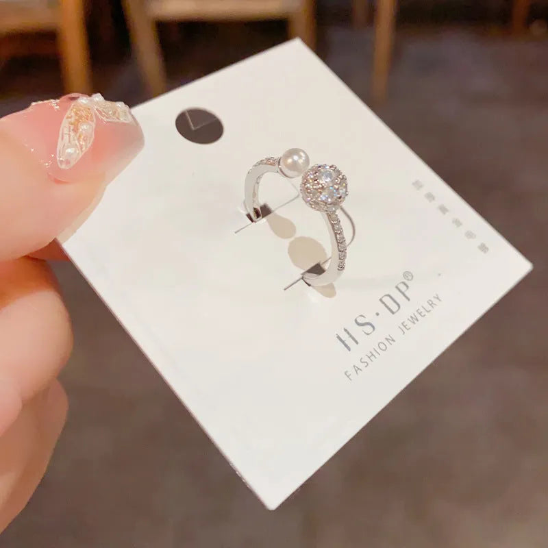 Open-end pearl ring with round zircon stone in gold or silver colour finish.