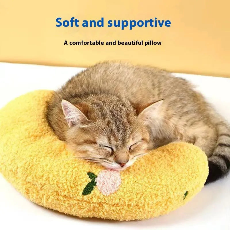 Blue and yellow U-shaped cat pillow in moon and question mark designs on a wooden floor.