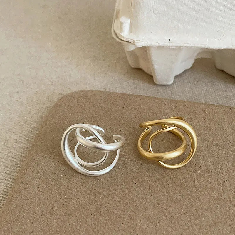 Geometric open ring with interlaced metal design and matte finish in gold colour.