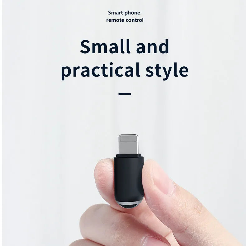 Small black capsule infrared emitter remote control for smartphones next to a phone.
