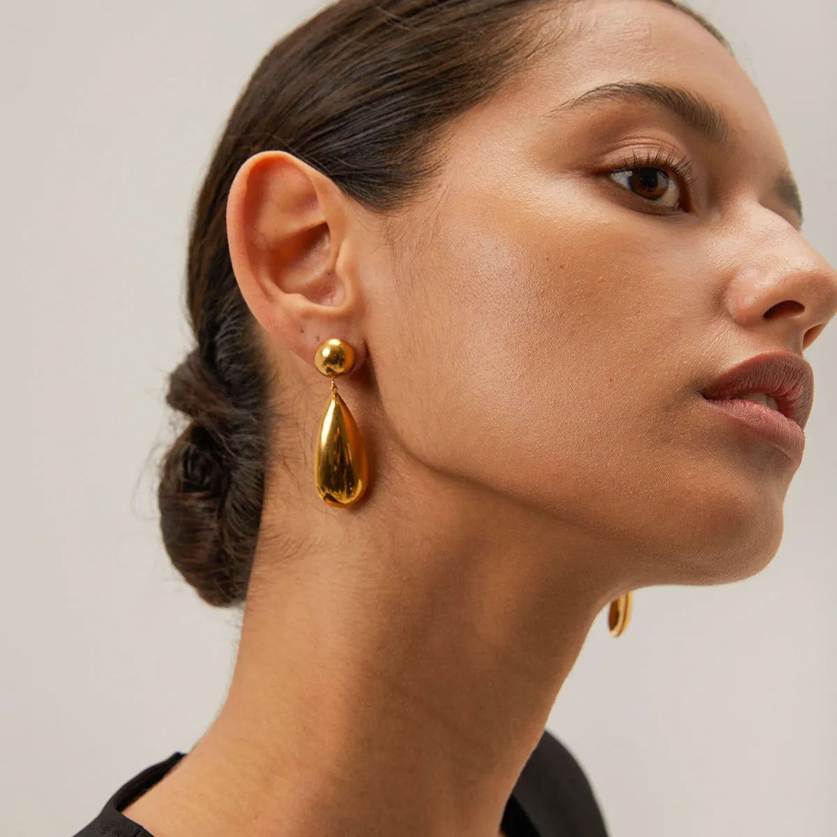 A pair of gold-coloured geometric hemisphere earrings with a hanging water droplet pendant.