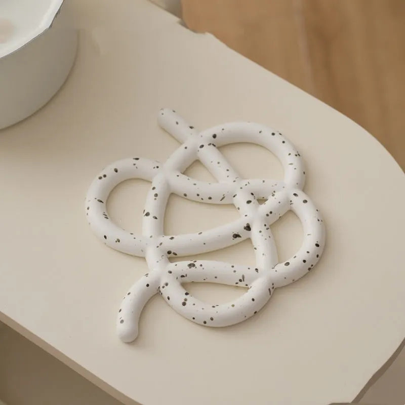 Irregular-shaped ceramic heatproof mat in a solid colour on a wooden table, protecting it from a hot pan.