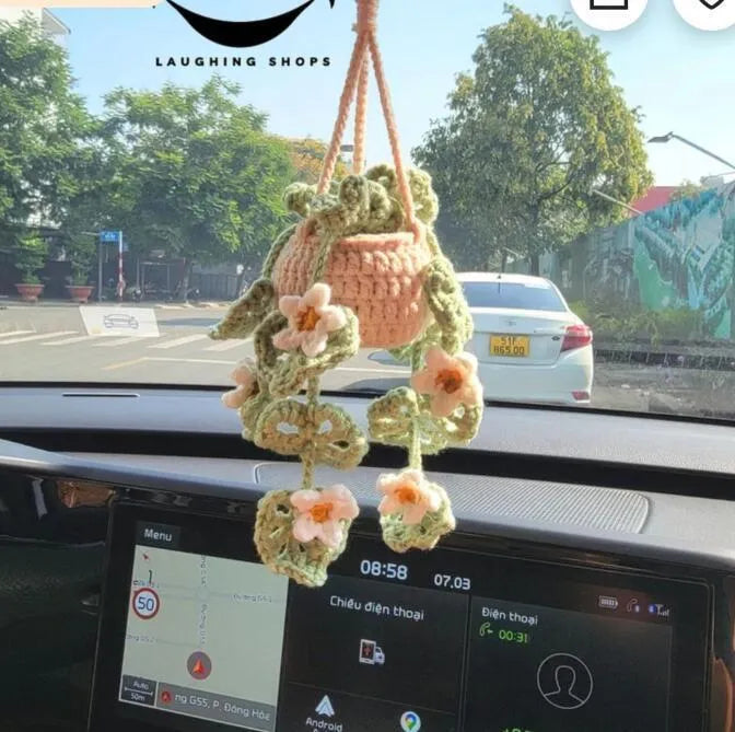 Green and white crocheted wool car plant decoration with a white hanging rope.