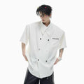 A man's loose-fitting short-sleeved casual shirt in a choice of black, blue, or white, showing lapel collar and metal decoration details.
