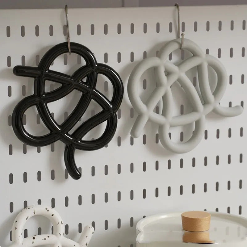 Irregular-shaped ceramic heatproof mat in a solid colour on a wooden table, protecting it from a hot pan.