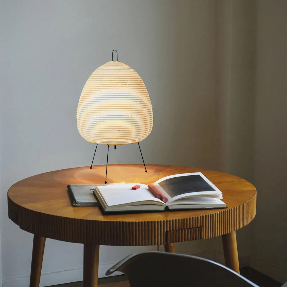 Japanese style table lamp with a white handmade rice paper lantern shade and aluminium base on a wooden table.
