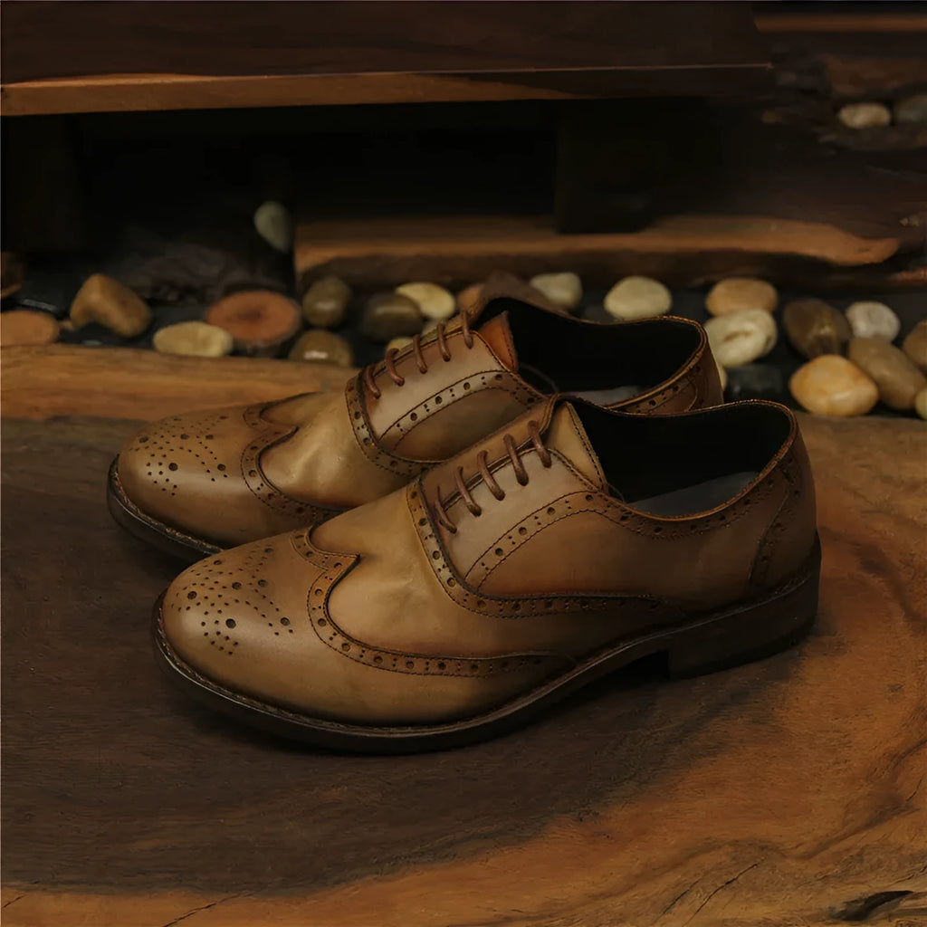 Men's light brown leather lace-up shoes with hand-carved distressed detailing on a wooden background.