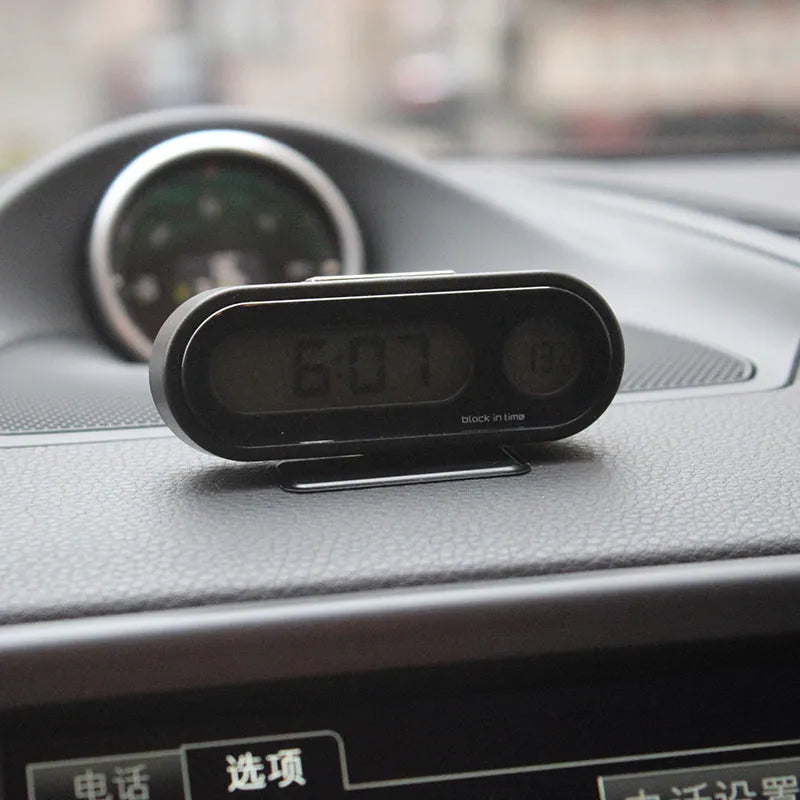 Black digital LED car clock and thermometer with adjustable mounting bracket on a dashboard.