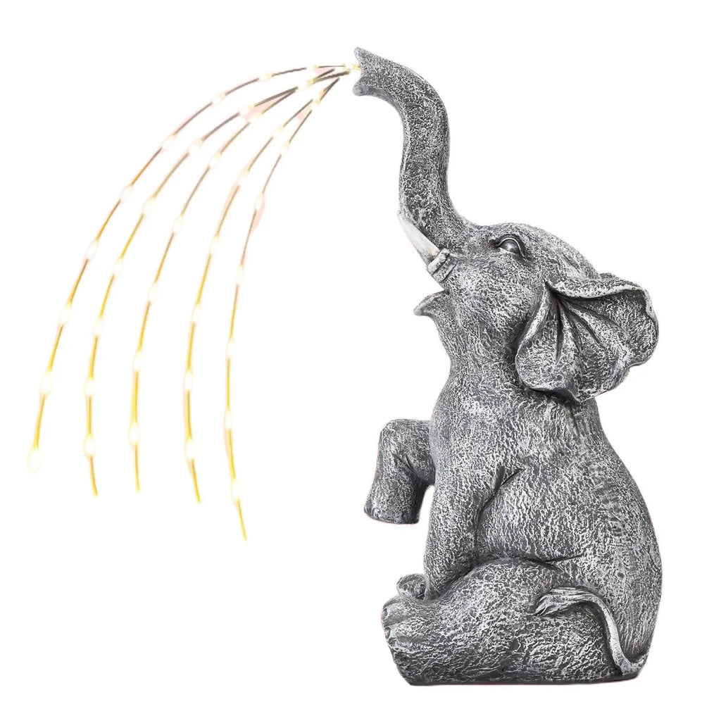 Grey resin elephant garden statue with warm white LED light glowing at its base on a patio.