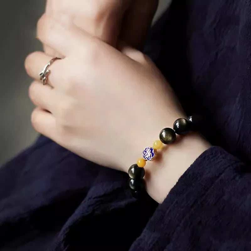 Golden obsidian bracelet with geometric beads and a detailed zodiac animal charm on a wrist.
