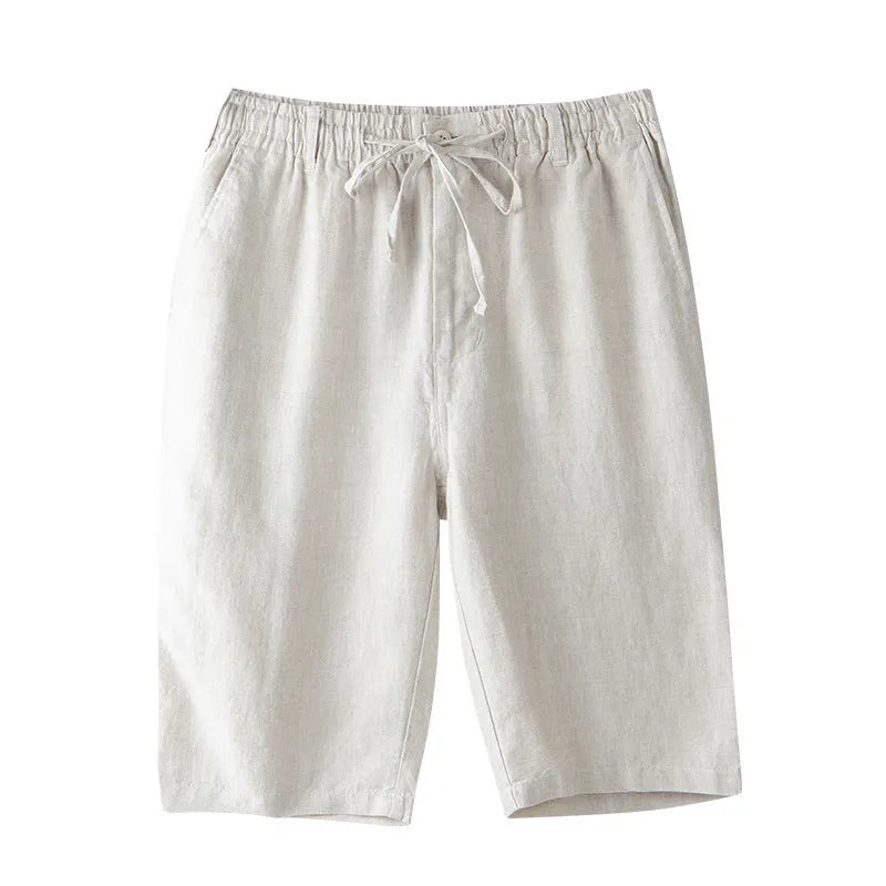 Man wearing light grey linen capri trousers with a loose, straight-leg fit on a beach.