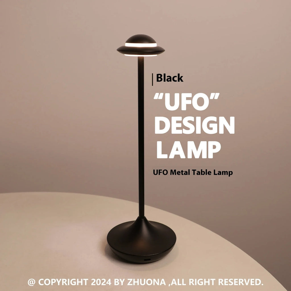 Modern UFO-shaped metal table lamp in black on a wooden desk, showing cord-free design.