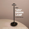 Modern UFO-shaped metal table lamp in black on a wooden desk, showing cord-free design.