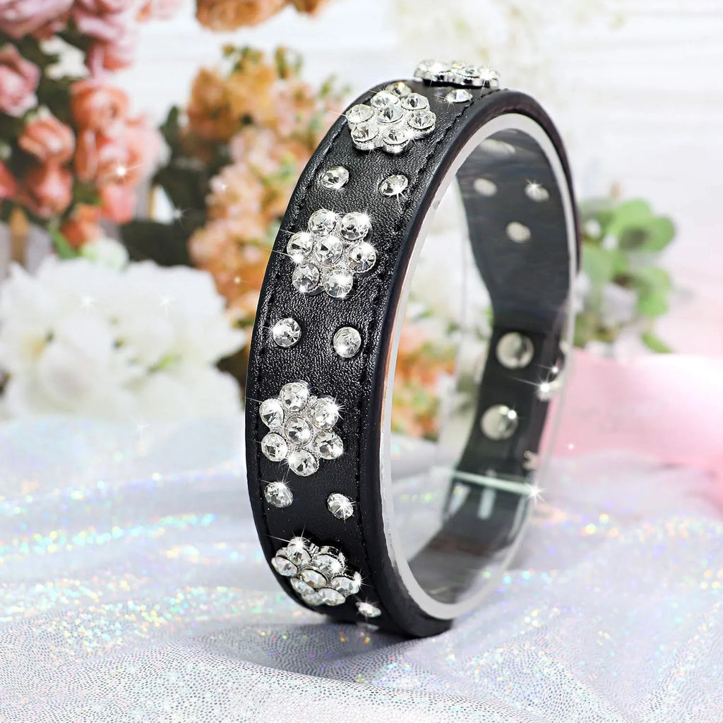 A black PU leather dog collar with a sparkling rhinestone flower pattern and metal studs, showing an adjustable metal buckle.