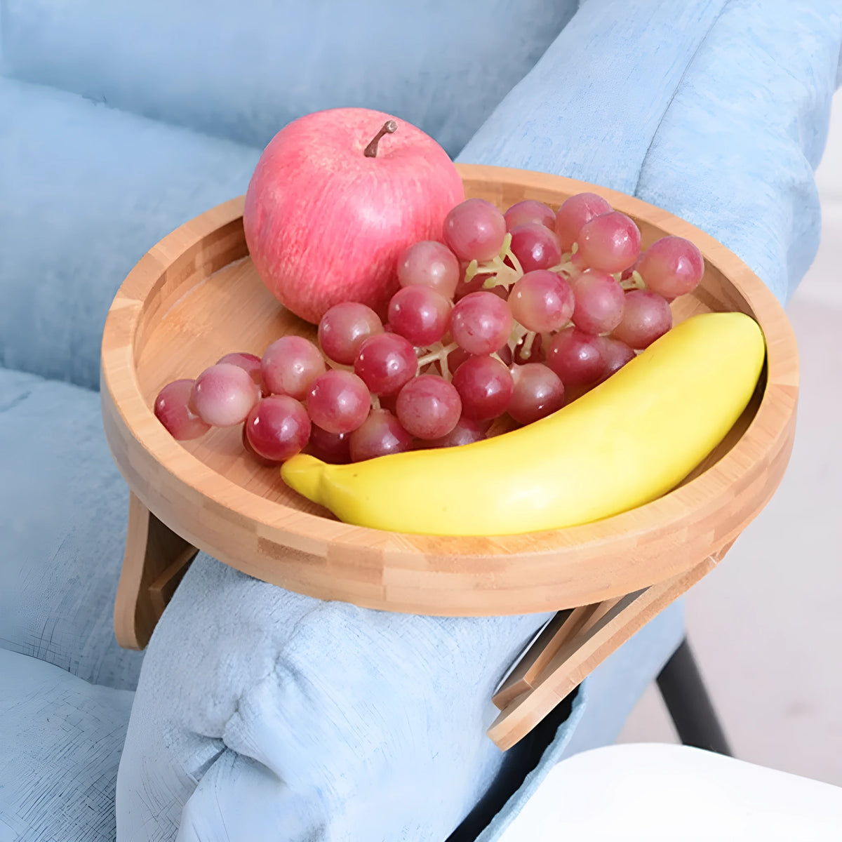 Wooden clip-on sofa tray table with carved surface in bamboo colour, attached to armrest holding snacks and remote
