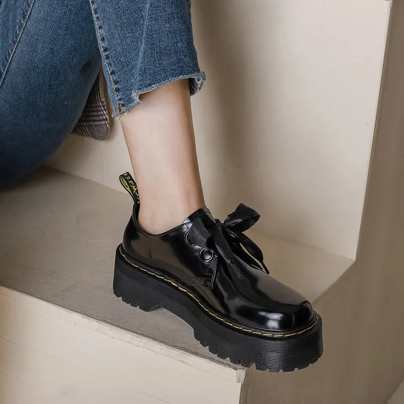 Black women's thick soled lace-up shoes with a cross-strap and ribbon detail on the front.