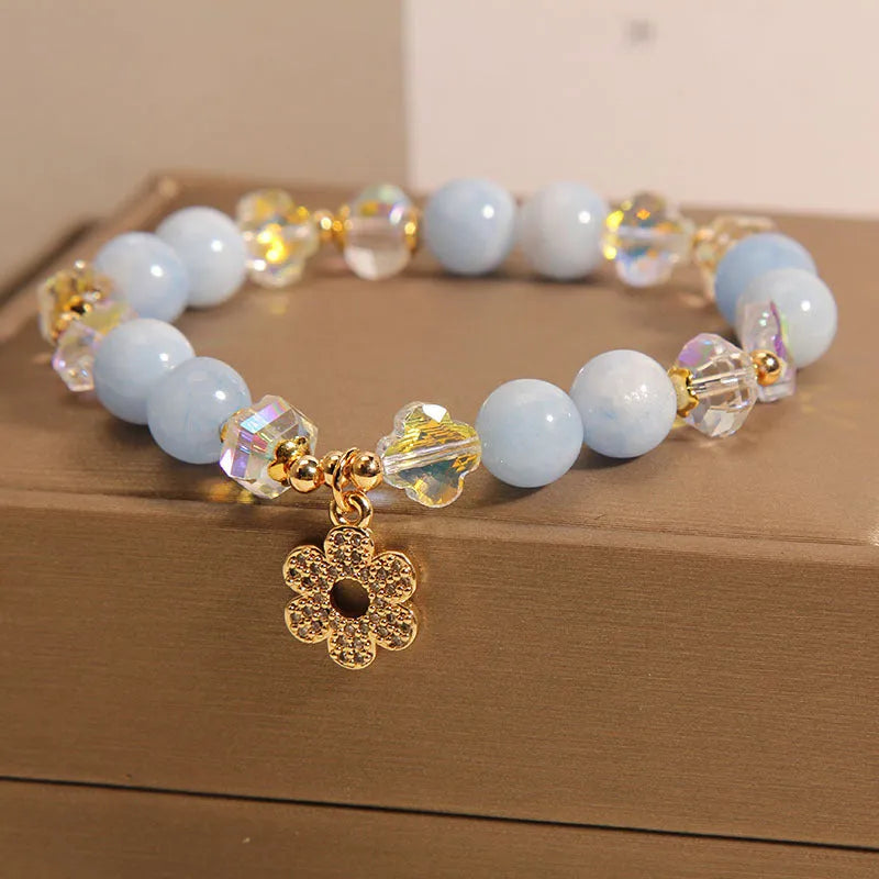 Women's aquamarine crystal bracelet with a four-leaf clover charm and pearl accent on wrist.